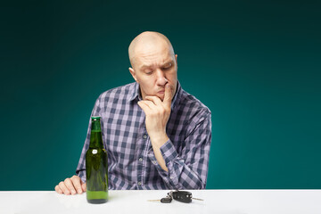 A man with bottle beer holds a car key and choosing ,drink alcohol or drive isolated over green background. Do not drink alcohol and drive concept.