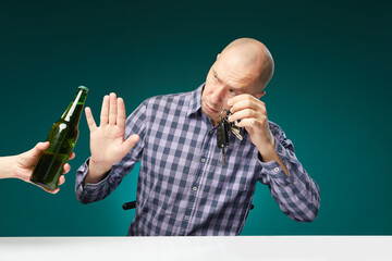 Man refusing alcohol beer showing car key as gesture of don't drink and drive isolated over green...