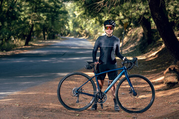 Obraz premium chica posando con bicicleta al lado de la carretera en medio del bosque, usando casco y lentes de sol