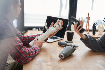 Male and female colleagues holding bionic prosthesis limbs and discussing it - obrazy, fototapety, plakaty