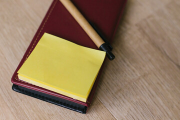 Fototapeta premium Leather notebook with yellow leaves. A paper pen lies next to it on a light wooden background.