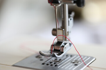 Close-up of red thread in sewing machine. Macro shot of metal details of equipment
