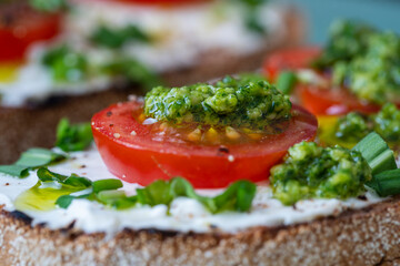 Delicious toasted bread with white cream cheese, green wild garlic and tomato on plate, close up