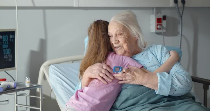 Little girl visiting and hugging sick grandmother in hospital ward