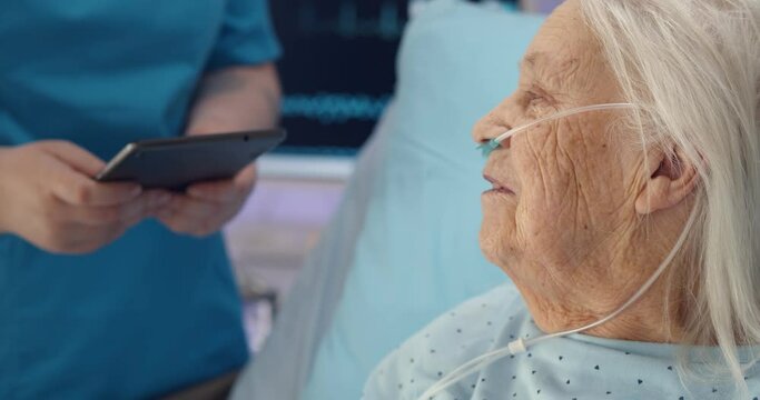 Close up of sic aged woman in hospital bed listening to doctor with digital tablet