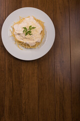 Pasta with bechamel sauce with grated cheese and parsley leaves served on a white plate. Top photo with bottom space for text.