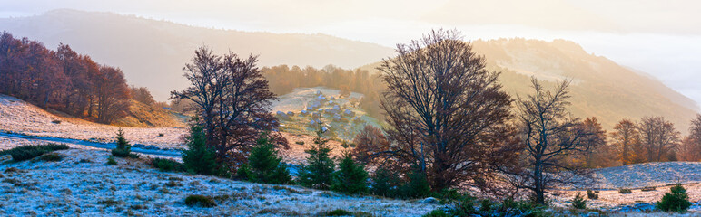 Autumn morning mountain panoramic view with sunbeams through haze and low clouds.