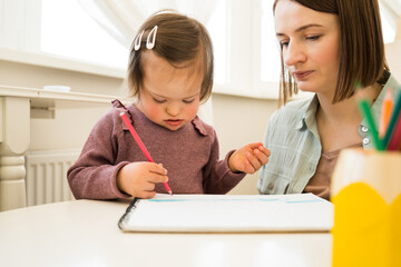 Child with down syndrome holding pencil and painting on the paper