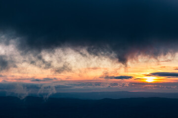 Sunset with sun hidden behind clouds over mountains and valley, with very low and close clouds