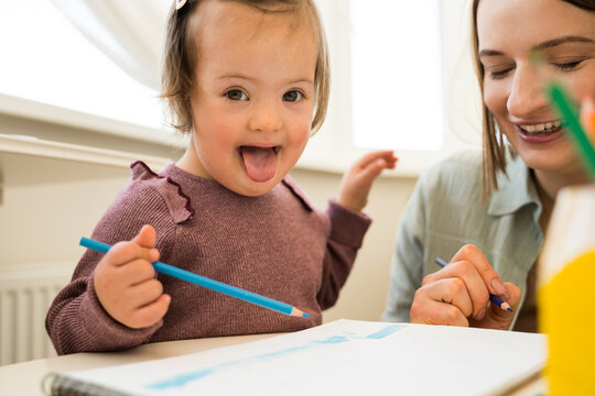 Girl with down syndrome drawing and sitting over a sheet of paper at the table