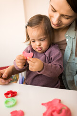 Girl with down syndrome holding plasticine while sculpting with her mother