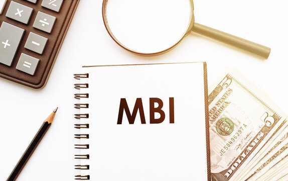 White notepad with the text of the MBI on the background of dollars and office tools.