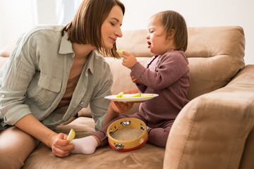 Girl with down syndrome feeding with sliced ​​apple her cute friendly mother