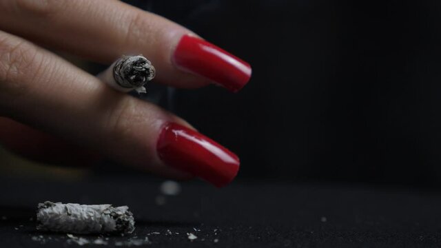 Close up shot of a woman's hand with red nails holding her burning cigarette
