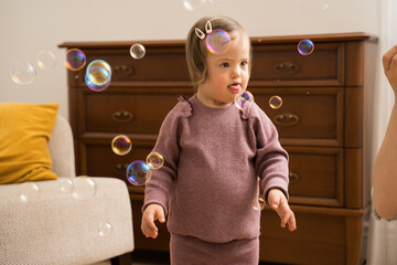 Girl with down syndrome looking while her friendly mother blowing soap bubbles