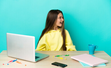 Little girl in a table with a laptop over isolated blue background laughing in lateral position