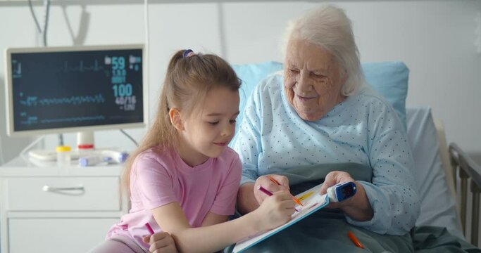 Little girl visiting grandmother in hospital bed painting together