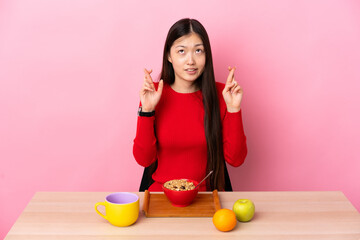 Young Chinese girl  having breakfast in a table with fingers crossing and wishing the best