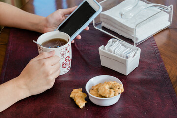 Young woman having a tea with cookies while checking her cell phone