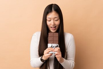 Young Chinese girl over isolated background eating a chocolate tablet