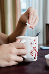 Woman's hands putting saccharin or sugar from an envelope into a tea or hot drink