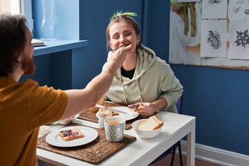 Back view of the bearded man feeding with a sandwich his color haired woman
