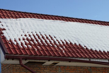 part of a private house from a red tile roof under white snow against a blue sky