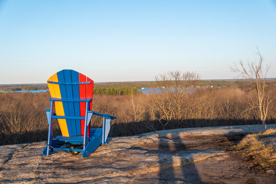 A lone, empty Muskoka (Adirondack) chair sits atop a rocky hill overlooking the surrounding forest at Walker's Point Lookout Trail near Gravenhurst, Ontario.