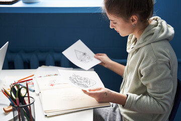 Woman holding sketches and looking on it while making choice at home