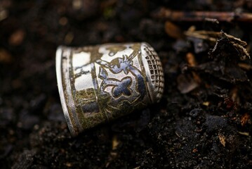 one antique silver thimble with patterns lies on black ground in the street