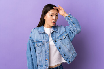 Young Chinese girl over isolated purple background doing surprise gesture while looking to the side