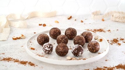 Homemade healthy raw vegetarian dessert energy balls with nuts, dates, peanut butter, cocoa powder, coconut flakes and oats on white plate with sunlight. Healthy eating. Fitness snack. Selective focus
