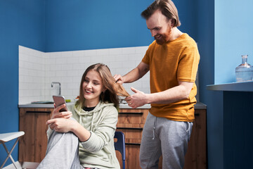 Man holding scissors and looking at his woman while cutting her hair