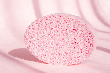 Pink porous sponge for bath on pink background with shadows. Spa, shower cleaning accessory