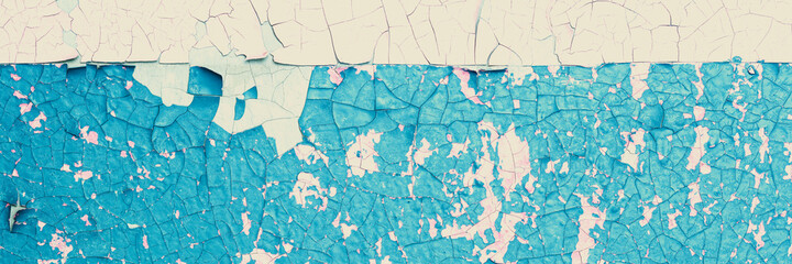 Peeling paint on the wall. Panorama of a concrete wall with old cracked flaking paint. Weathered rough painted surface with patterns of cracks and peeling. Panoramic texture for background and design.