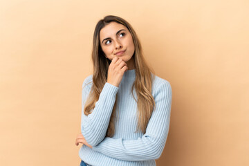 Young caucasian woman isolated on beige background and looking up