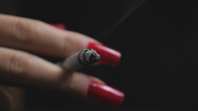 A woman with red nails holding her burning cigarette isolated on a black background
