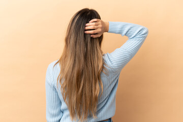 Fototapeta premium Young caucasian woman isolated on beige background in back position and thinking