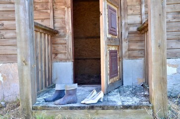 An old pair of white shoes on the doorstep of an old house. An old pair of boots on the doorstep of a wooden house. Shoes at the entrance to an old wooden house.