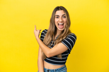 Young caucasian woman isolated on yellow background surprised and pointing side