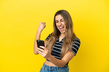 Fototapeta premium Young caucasian woman isolated on yellow background with phone in victory position