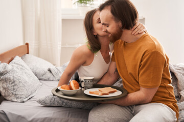Man bringing breakfast of the toasts, donuts and coffee at bed to his loving woman