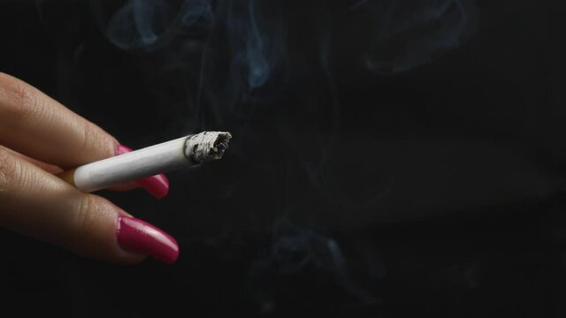 A woman with red nails holding her burning cigarette isolated on a black background