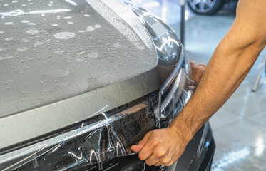 Car protection film or PPF process of wrapping and installing on car hood by detailer worker hands, close up.