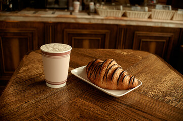 Croissant with coffee to go in a paper cup, take away breakfast