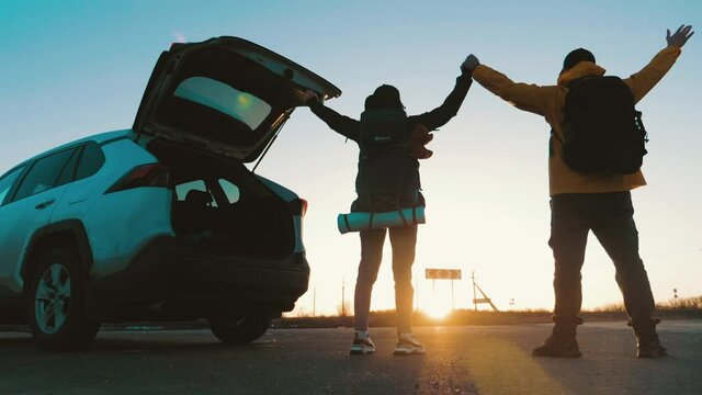 Free travelers. Couple silhouette tourists with backpacks next to car, discussing the trip. Family trip together by car during summer holidays. Happy young family travel by car. Vacations concept.