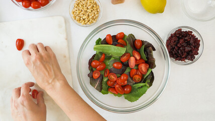 Lettuce salad with fresh cherry tomatoes, dry cranberries, nuts, and honey mustard salad dressing recipe. Close up view from above, woman hands