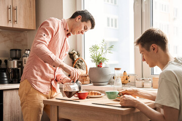 Fototapeta na wymiar Gay wearing shirt pouring coffee to cup for breakfast for him and his boyfriend