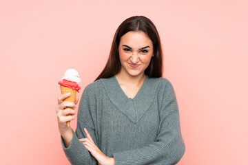 Young woman holding a cornet ice cream isolated on pink background with sad expression