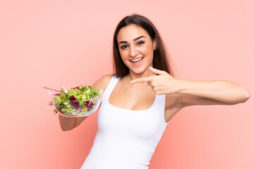 Young caucasian woman holding a salad isolated on pink background